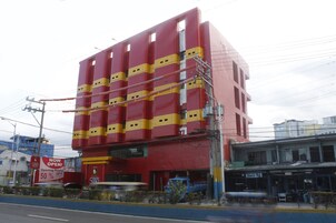 Un edificio de varios pisos con fachada roja y amarilla, entrada visible y un letrero que indica un 50% de descuento por inauguración.