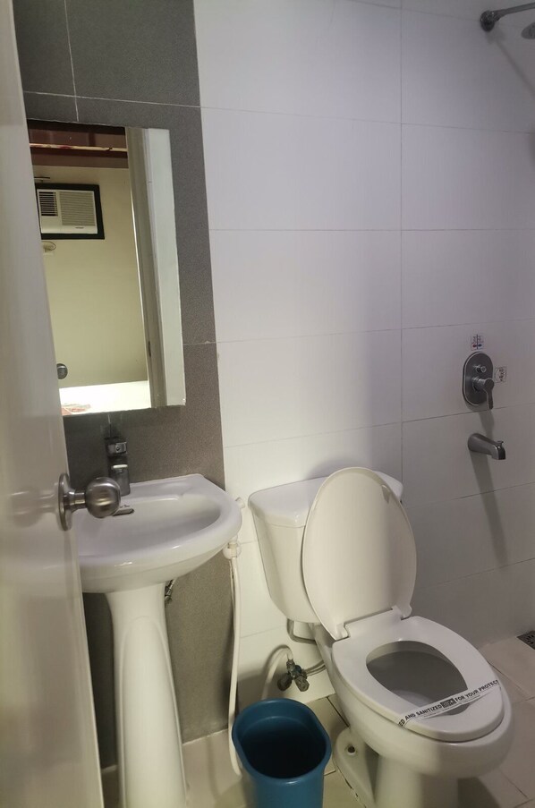 Une salle de bain avec des toilettes blanches, un lavabo et un seau bleu.