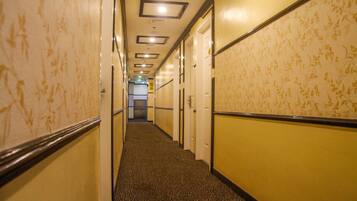 A hotel hallway with patterned walls, carpeted floors, and doors leading to rooms.