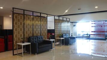 A modern lobby with a black leather sofa, a red chair, and a glass partition with intricate patterns.