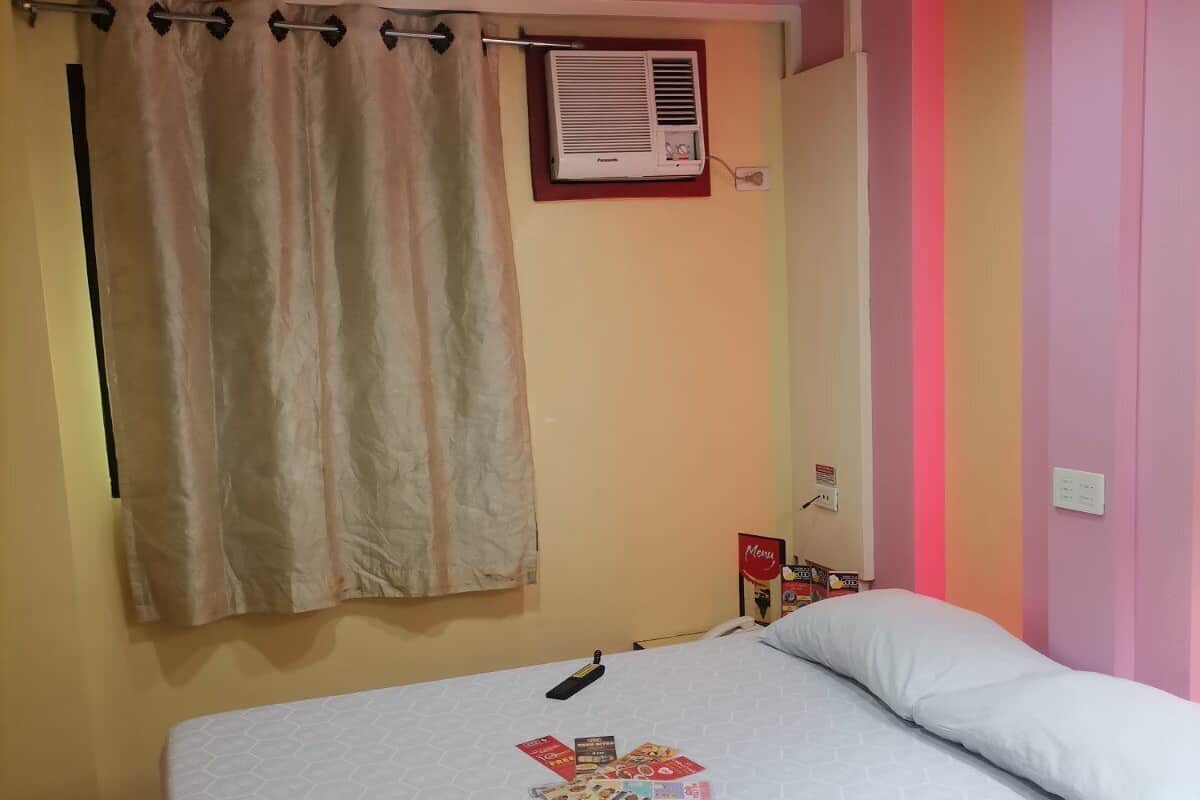 Een slaapkamer met een bed, een gordijn, een airconditioner en een wand met een bloemenprint.