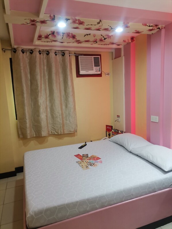 A bedroom with a bed, a curtain, an air conditioner, and a wall with a floral pattern.