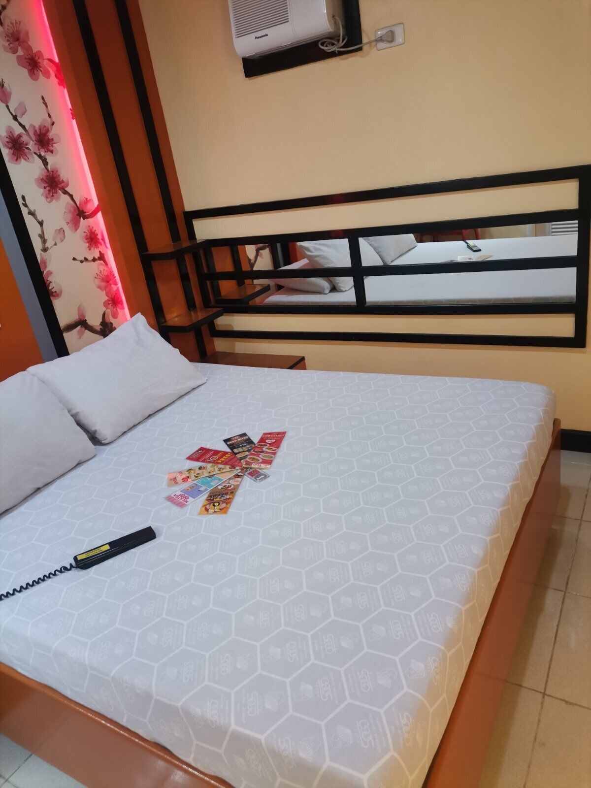 A hotel room with a bed, a headboard, a wall-mounted air conditioner, and a window with a view.