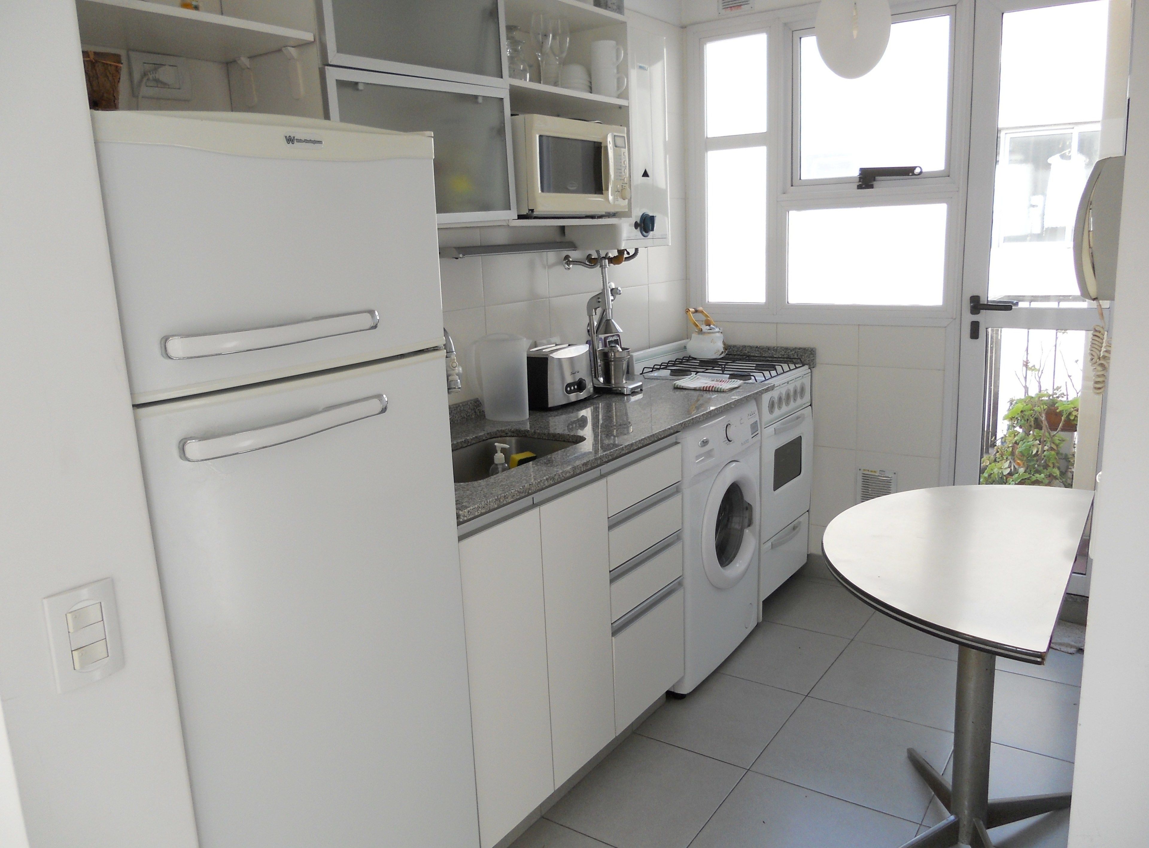 A kitchen with a refrigerator, microwave, toaster, kettle, sink, and washing machine.
