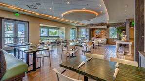 Ein geräumiges Restaurant mit mehreren Tischen und Stühlen, einer Theke mit Speisekarte und großen Fenstern, die einen Ausblick nach draußen bieten.
