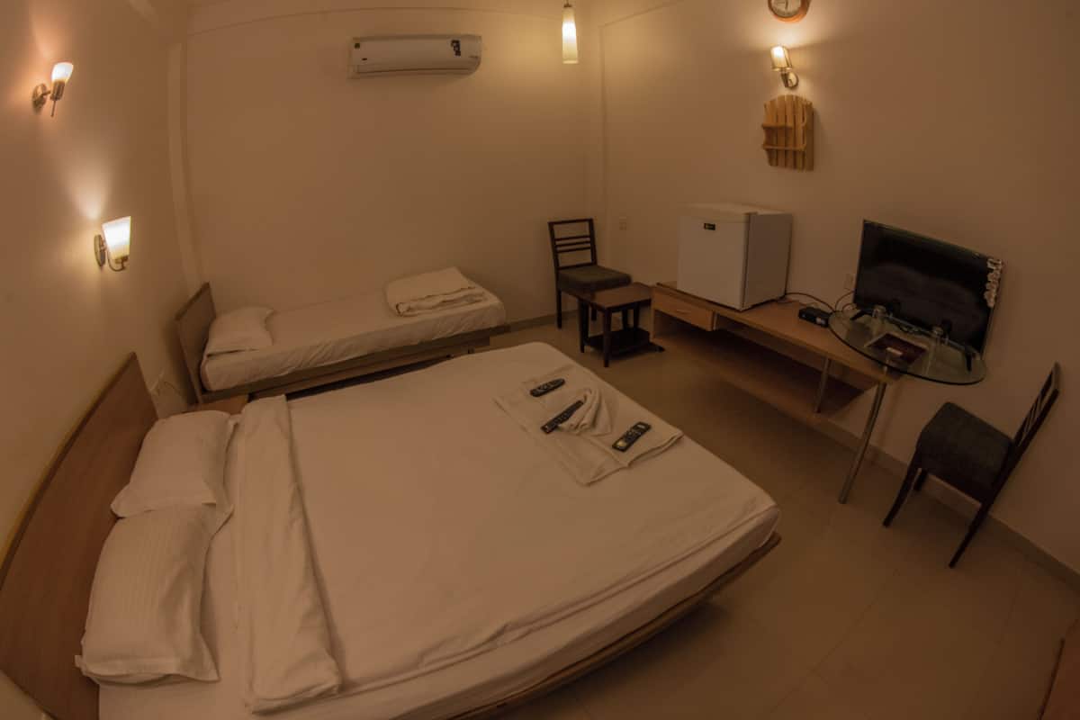 A hotel room with a large bed, a desk with a computer, a chair, a small table, and a TV.