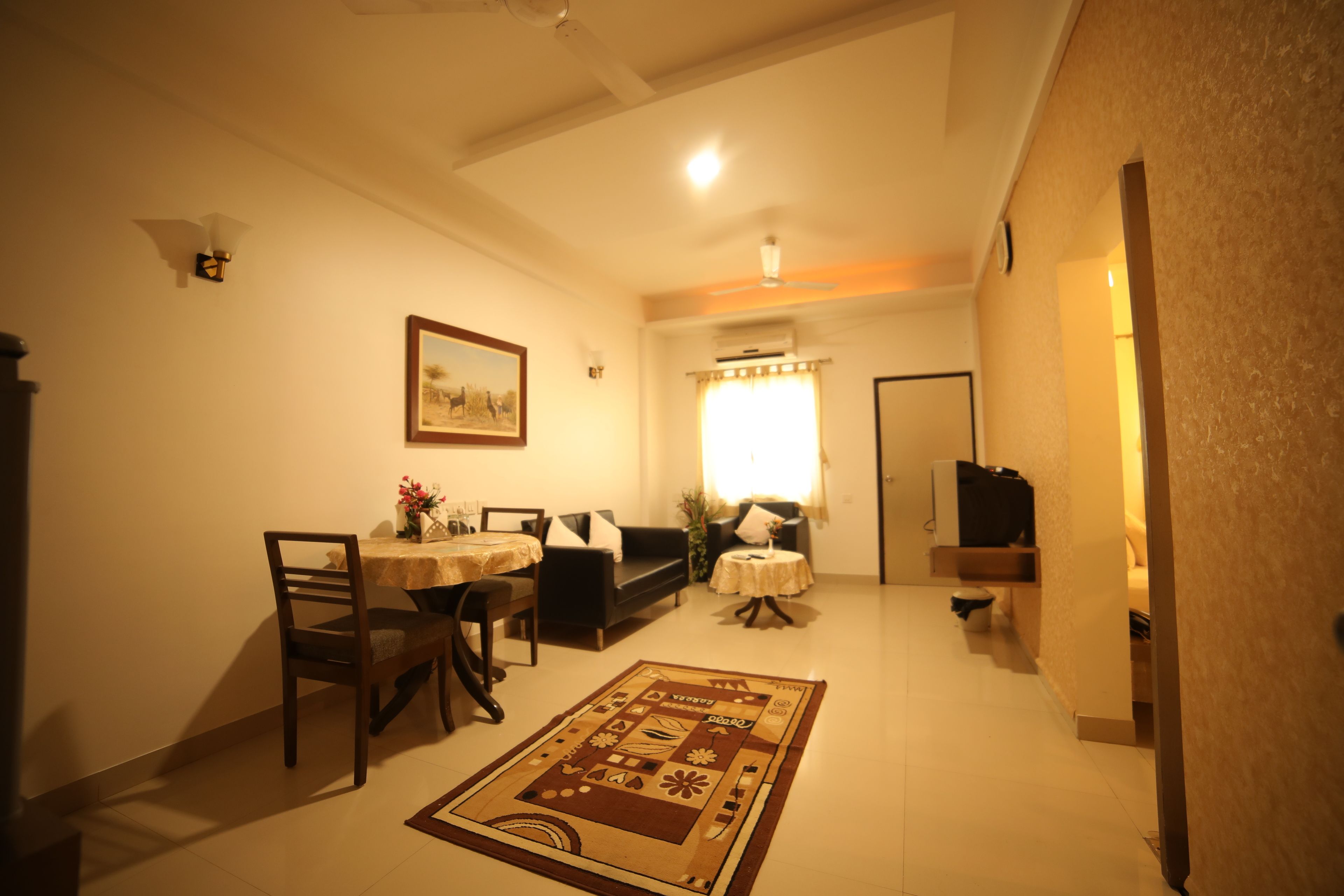 A dining area with a table, chairs, and a rug. There is a sofa and a small table with a lamp.