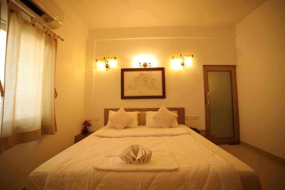 A hotel room with a large bed, two bedside tables, a nightstand, a framed artwork above the bed, and a door with a frosted glass panel.