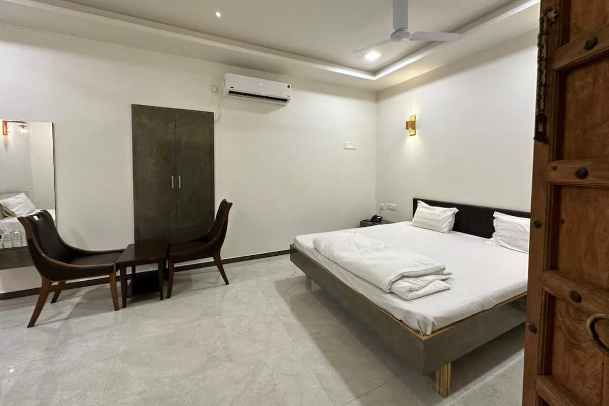 A hotel room with a bed, a desk, a chair, an air conditioning unit, and a wardrobe.