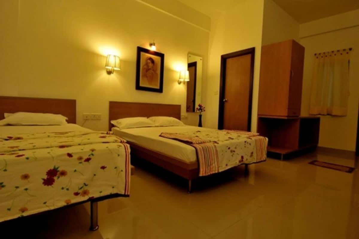 A hotel room with three beds, a wooden wardrobe, and two wall-mounted lamps.