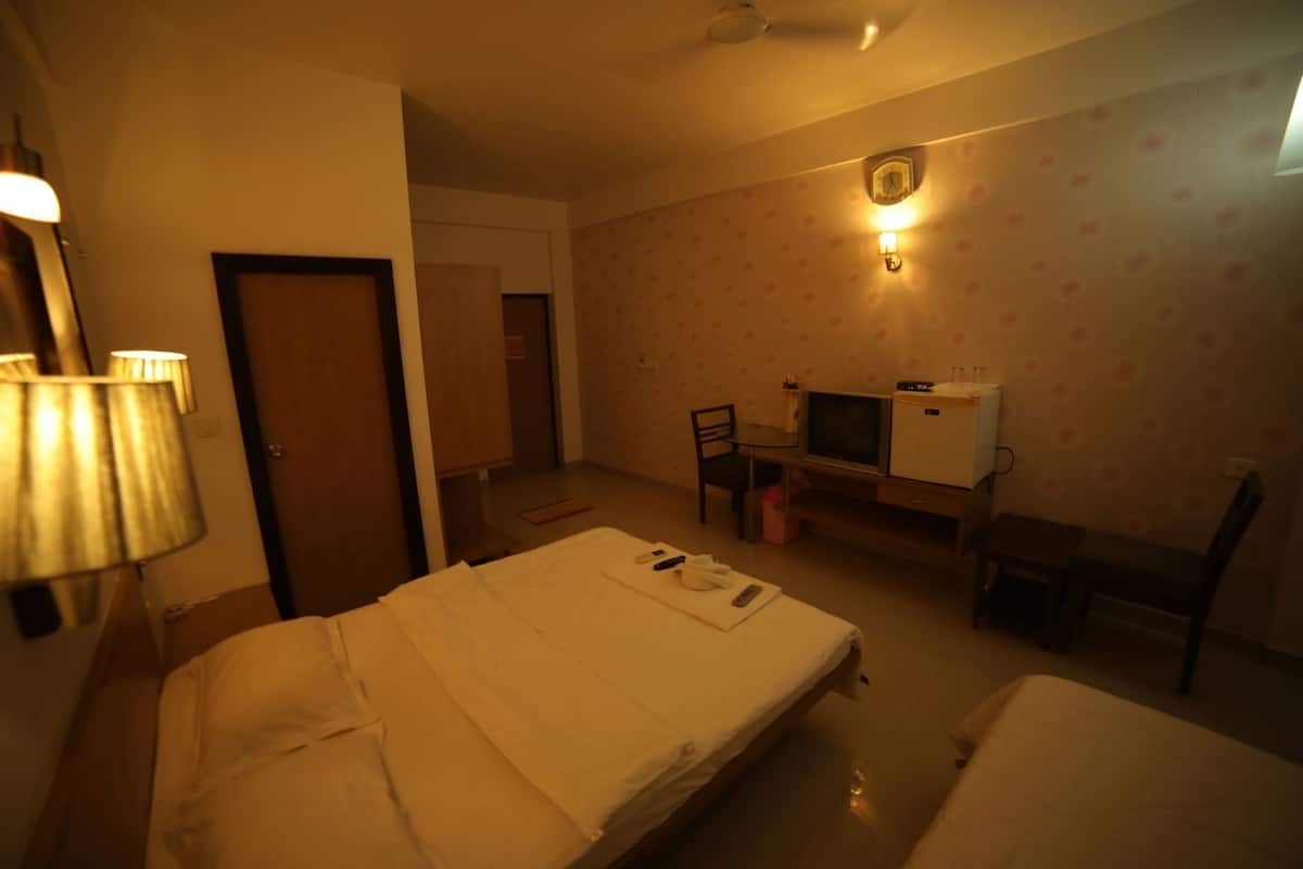A hotel room with a bed, a desk with a television, a chair, and a clock on the wall.