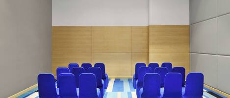 Una sala de conferencias con filas de sillas azules, un panel de pared de madera y una alfombra a rayas.