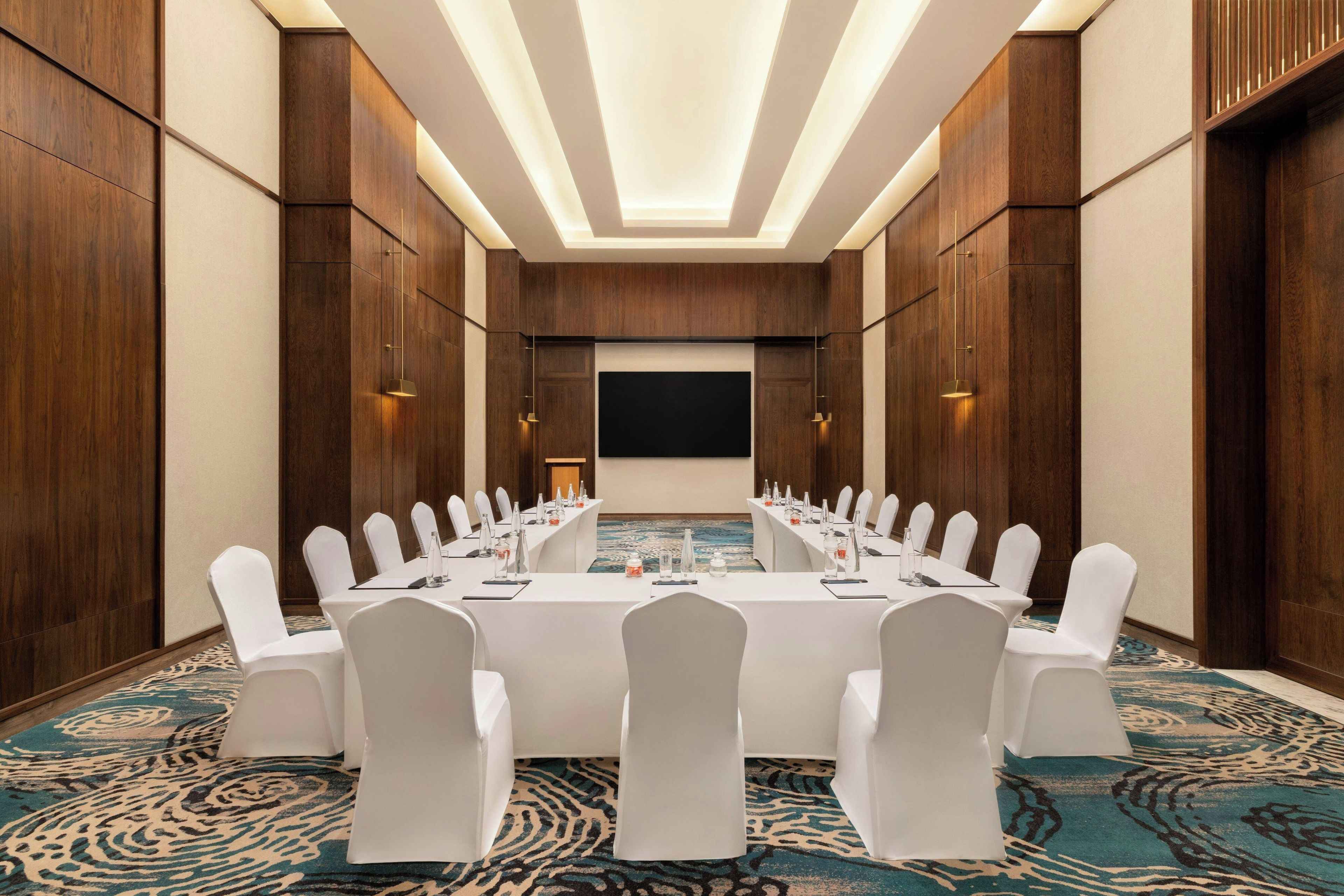 A conference room with a long table, white chairs, and a projector screen.