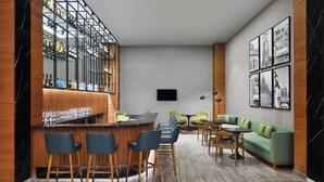 Zona de bar moderna con suelo de mármol, detalles de madera y un sofá verde en la zona de estar.