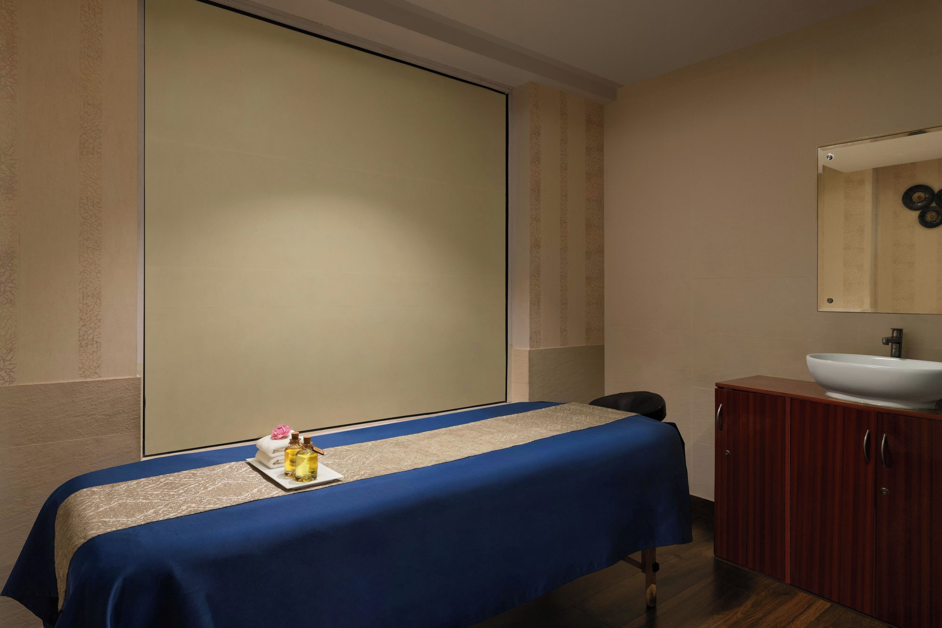 Una habitación con una mesa de masaje, un mueble de madera con un lavabo y un espejo grande.