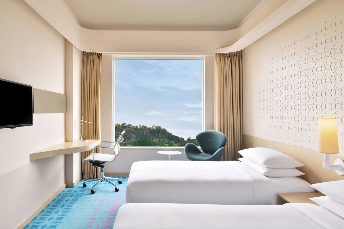 Ein Hotelzimmer mit Bett, Sessel, Fernseher und Fenster mit Blick ins Freie.