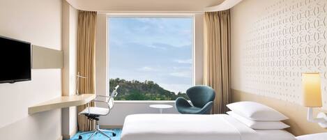 Habitación de hotel con cama, una silla, televisión y ventana con vista al exterior.