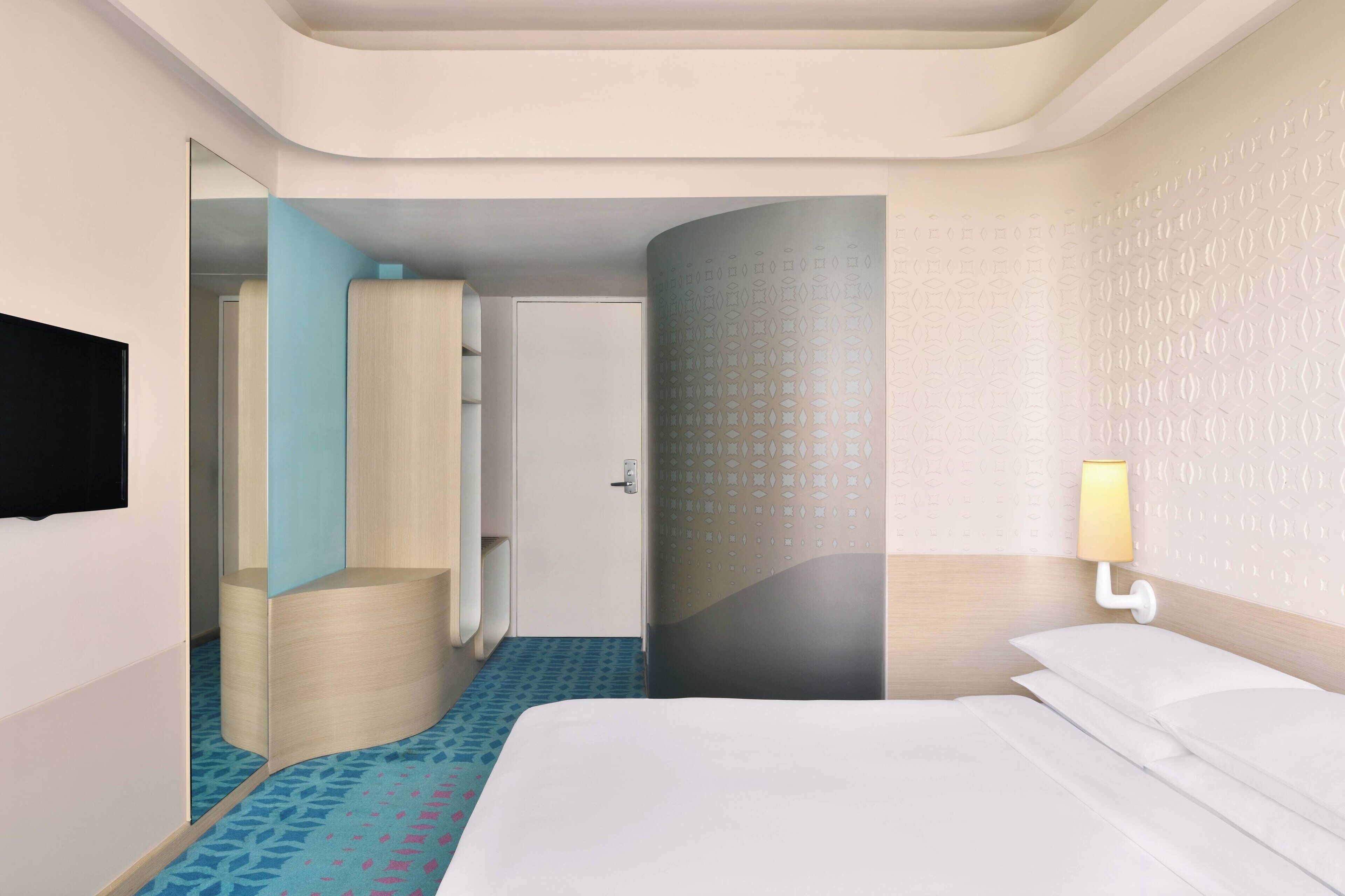Habitación de hotel con cama, televisor montado en la pared, baño con espejo y pared decorada.