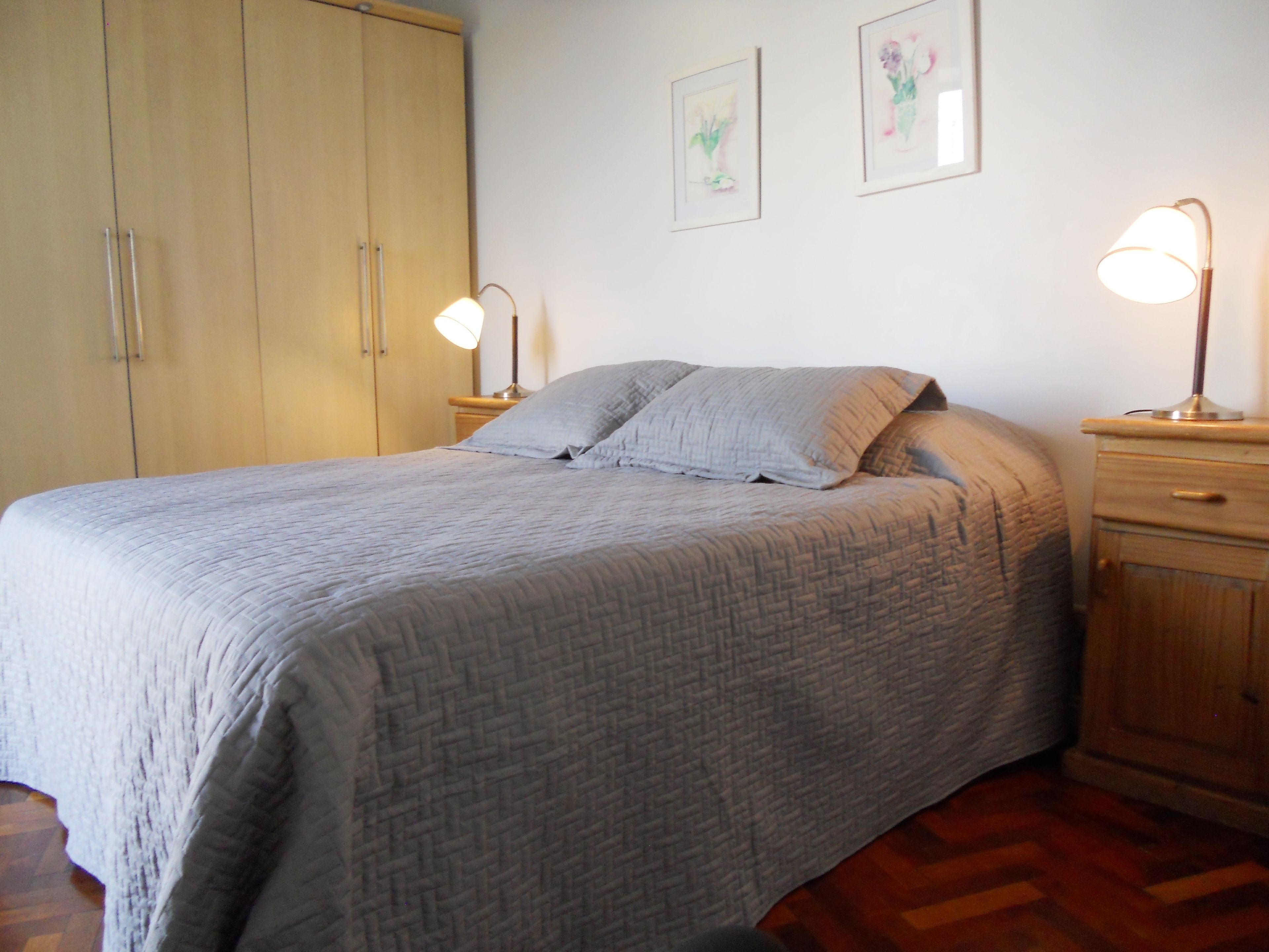 A bedroom with a bed, two bedside tables, a wardrobe, and two wall-mounted lamps.