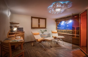 A cozy room with a wooden desk, two lounge chairs, a ceiling light, a window with a view, and a radiator.