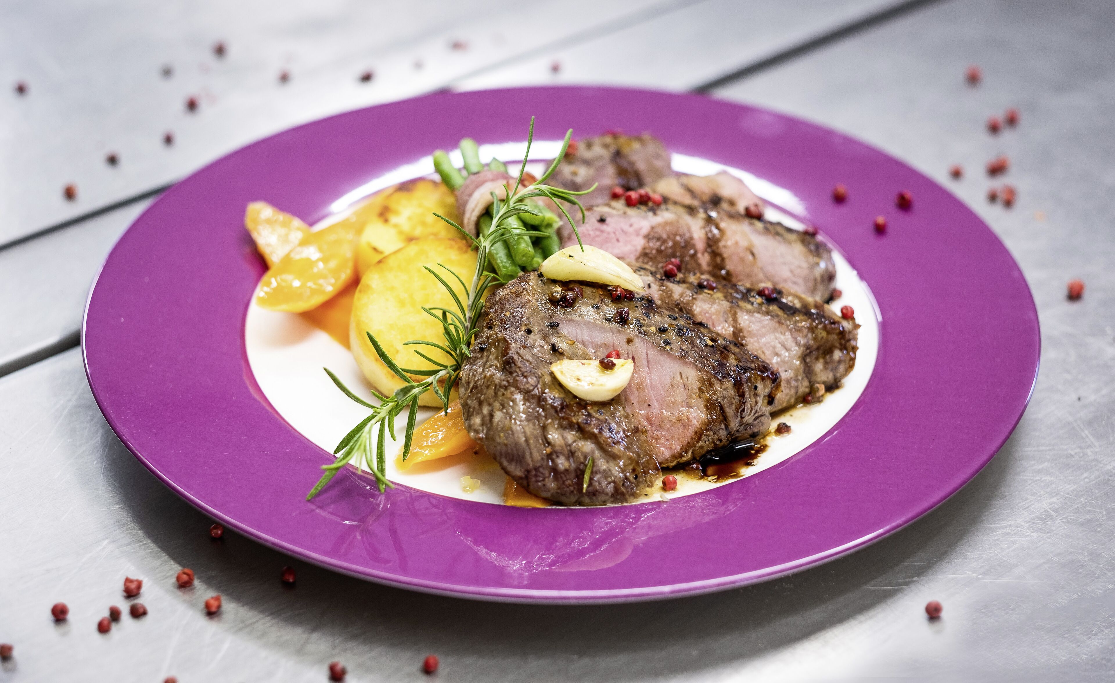 Une assiette de steak accompagnée de légumes et d’herbes, le tout présenté sur une assiette violette.