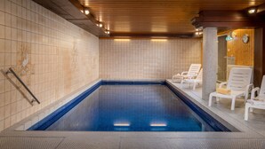 A swimming pool with tiled walls and wooden ceiling, surrounded by white lounge chairs. - Hotel Sonnenhof (Neuweiler)