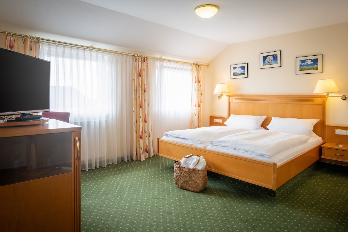 A hotel room with a bed, a desk with a television, a lamp, and a wall with framed pictures.