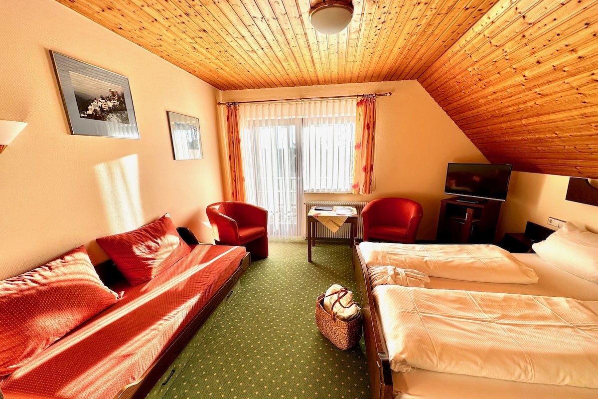 A hotel room with a wooden ceiling, two beds, a sofa, a chair, a table, and a television.