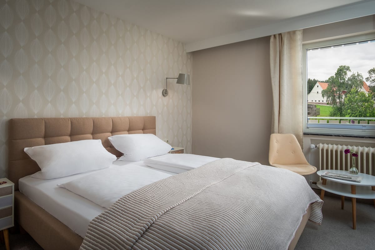 A hotel room with a bed, bedside tables, a chair, a window with a view, and a radiator.