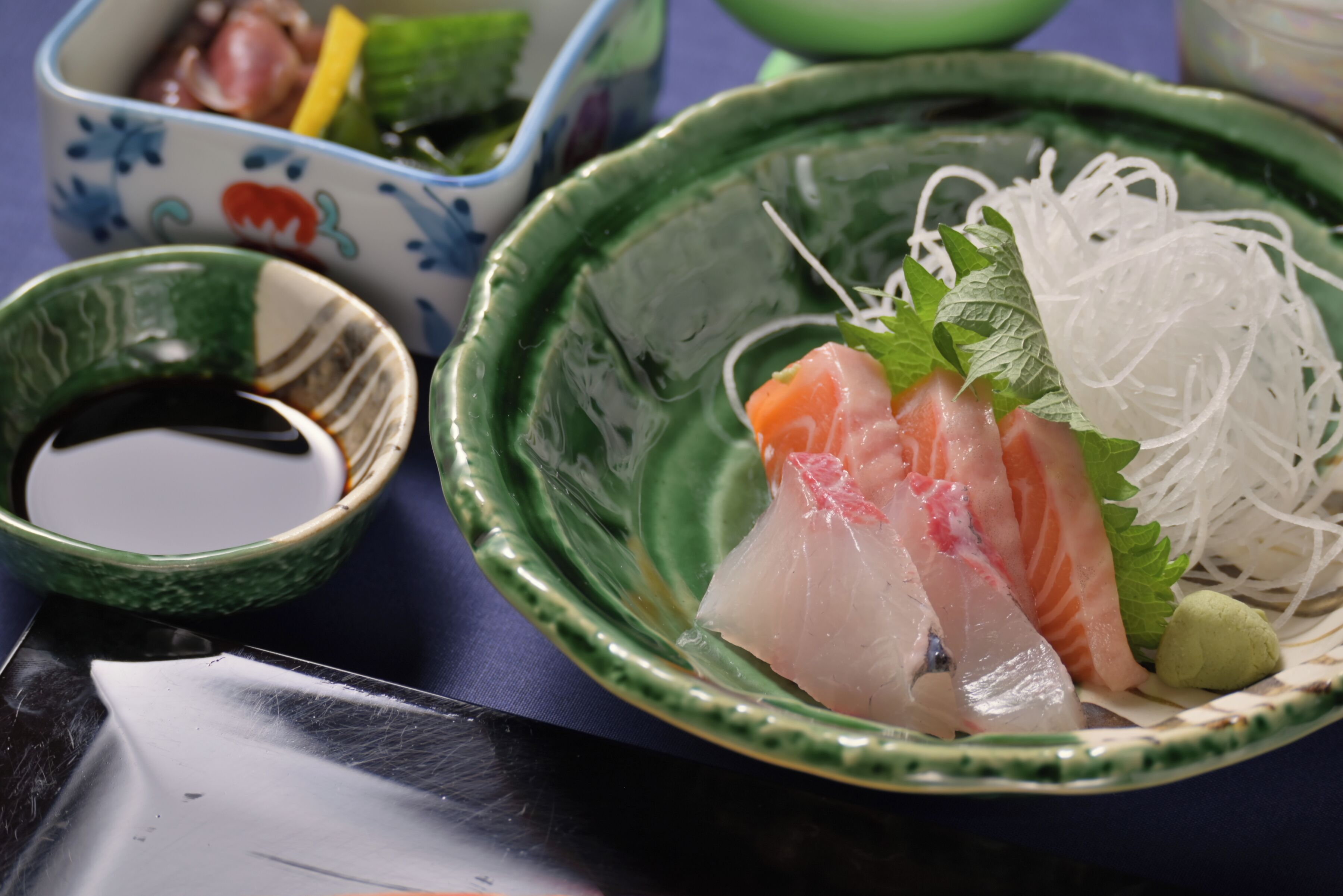 Un bol de sashimi acompañado de salsa de soja y verduras encurtidas.