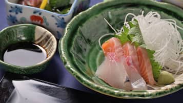 Un bol de sashimi acompañado de salsa de soja y verduras encurtidas.
