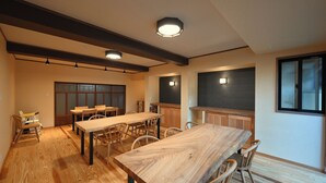 Un comedor amplio con una larga mesa de madera y sillas, una zona de cocina con armarios de madera, y un ventanal que proporciona luz natural.