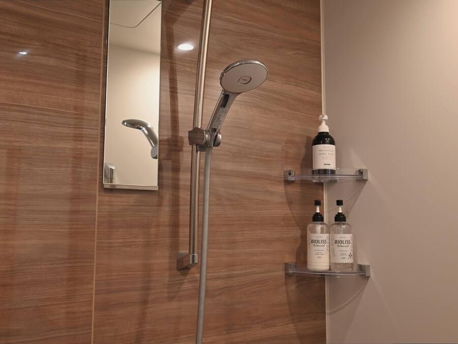 Ein modernes Badezimmer mit einer Holzvertäfelung, einer Handbrause und zwei Flaschen Bioliss Body Wash auf einem Regal.