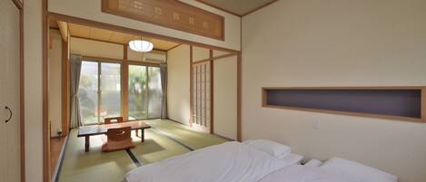 Una habitación japonesa tradicional con suelo de tatami, una cama de madera baja, una puerta corredera y vistas al exterior.