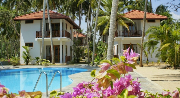 A resort with a swimming pool, two-story buildings with balconies, and palm trees. - Good Karma Ayurvedic Resort (Rekawa)