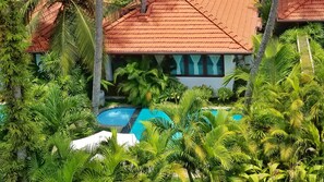 A tropical resort with a swimming pool surrounded by lush greenery and a building with a red-tiled roof. - Good Karma Ayurvedic Resort (Rekawa)