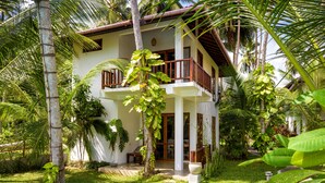 Un bâtiment à deux étages doté d’un balcon, entouré d’une végétation tropicale luxuriante.
