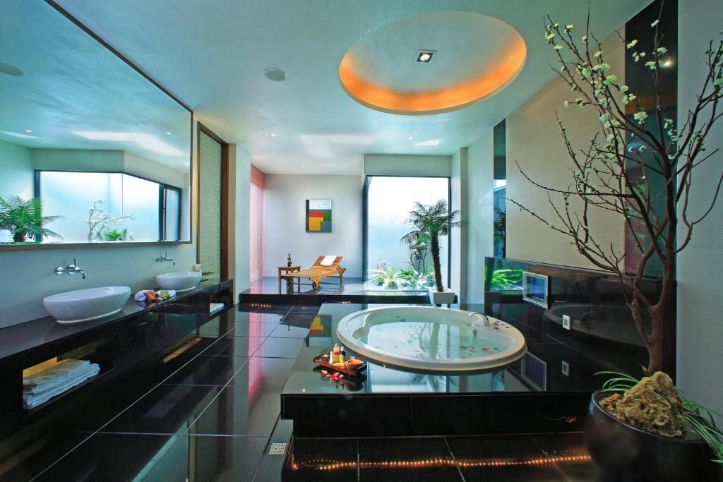 Un baño moderno con una bañera grande, dos lavamanos y una zona de estar con vistas al exterior.