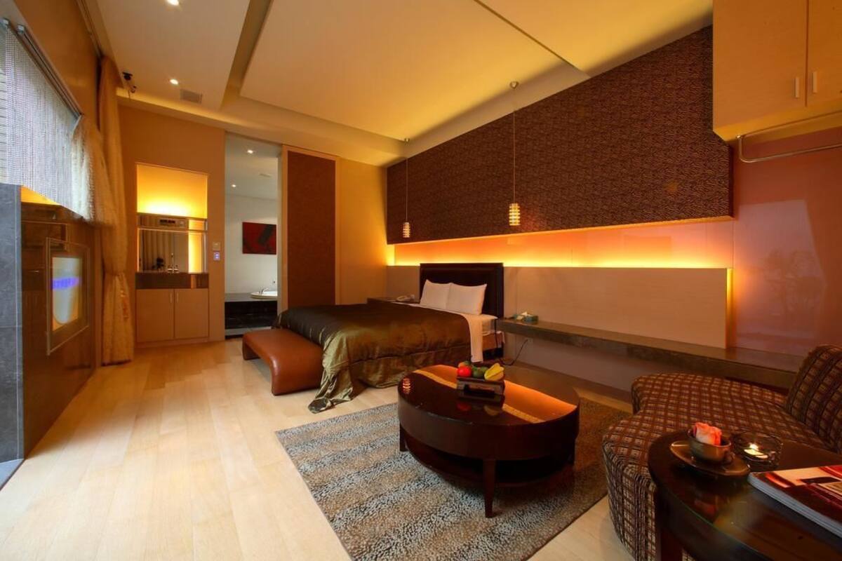 A modern hotel room with a bed, a seating area, a small table, and a television.