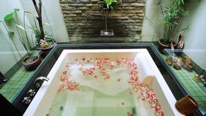 Een groot bad gevuld met water en rozenblaadjes, omringd door potplanten en een stenen muur.