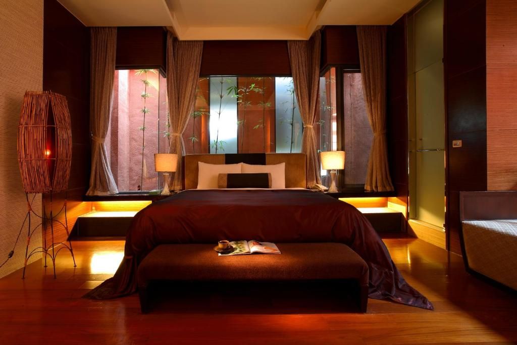 Een hotelkamer met een groot bed, bedlampen, een nachtkastje en een raam met gordijnen.