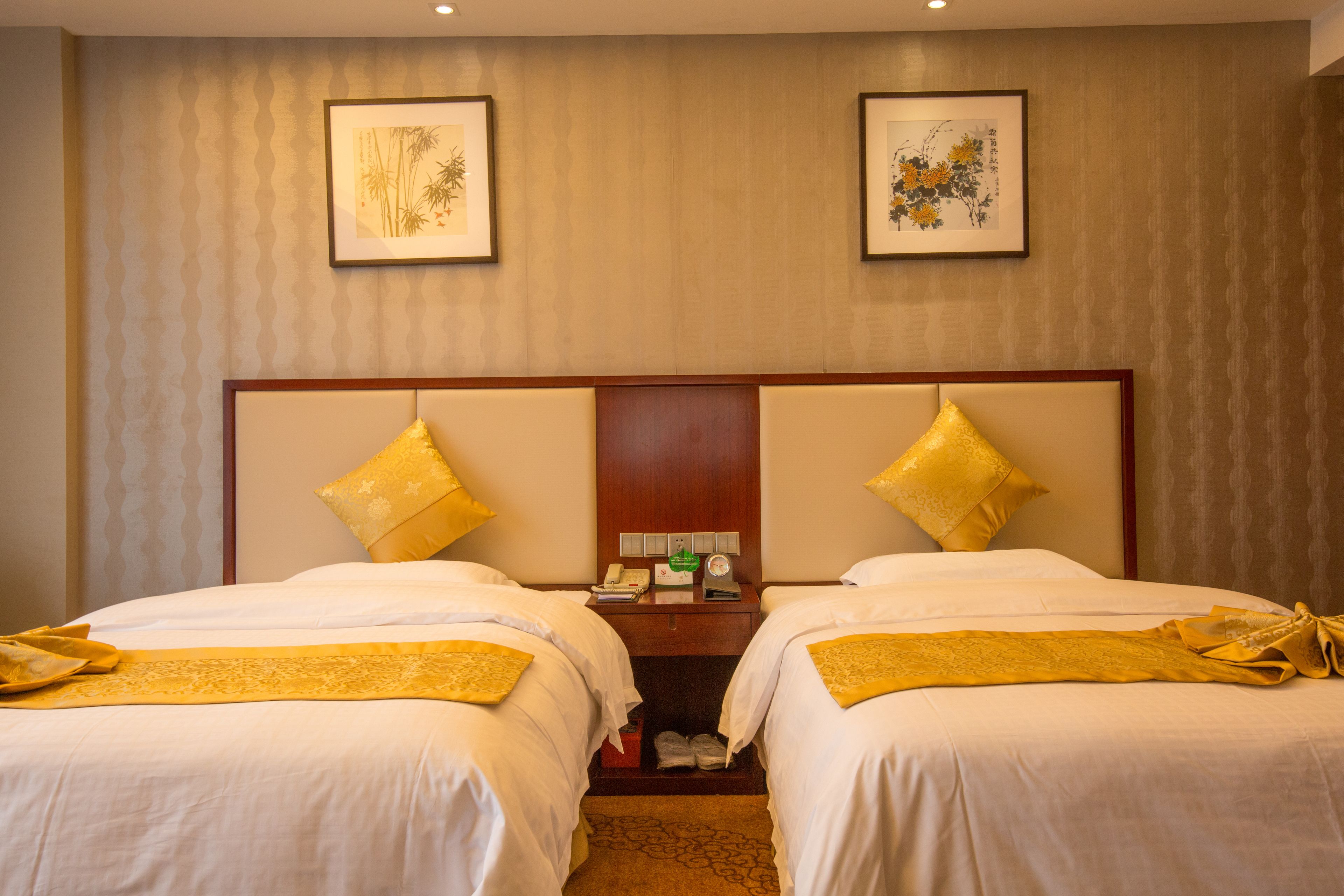A hotel room with two beds, a wooden headboard, and two framed artworks on the wall.