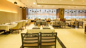 A spacious restaurant with multiple tables and chairs, large windows, and pendant lighting. - Loudi Huatian Hotel (Loudi)