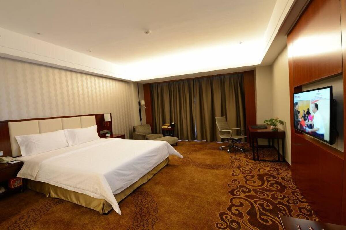A hotel room with a large bed, a desk with a chair, a television, and a carpeted floor.