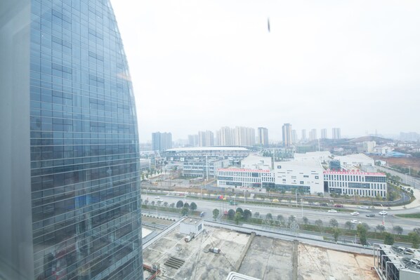 A high-rise building with a modern glass facade, a large open plaza with a few trees, and a busy road with vehicles. - Loudi Huatian Hotel (Loudi)