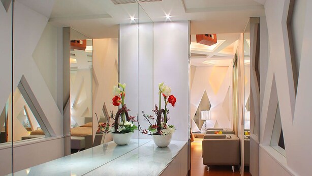 A modern hotel corridor with a reflective floor, a potted plant with flowers, a seating area, and a digital control panel on the wall. - Spring Hotel (Taichung)