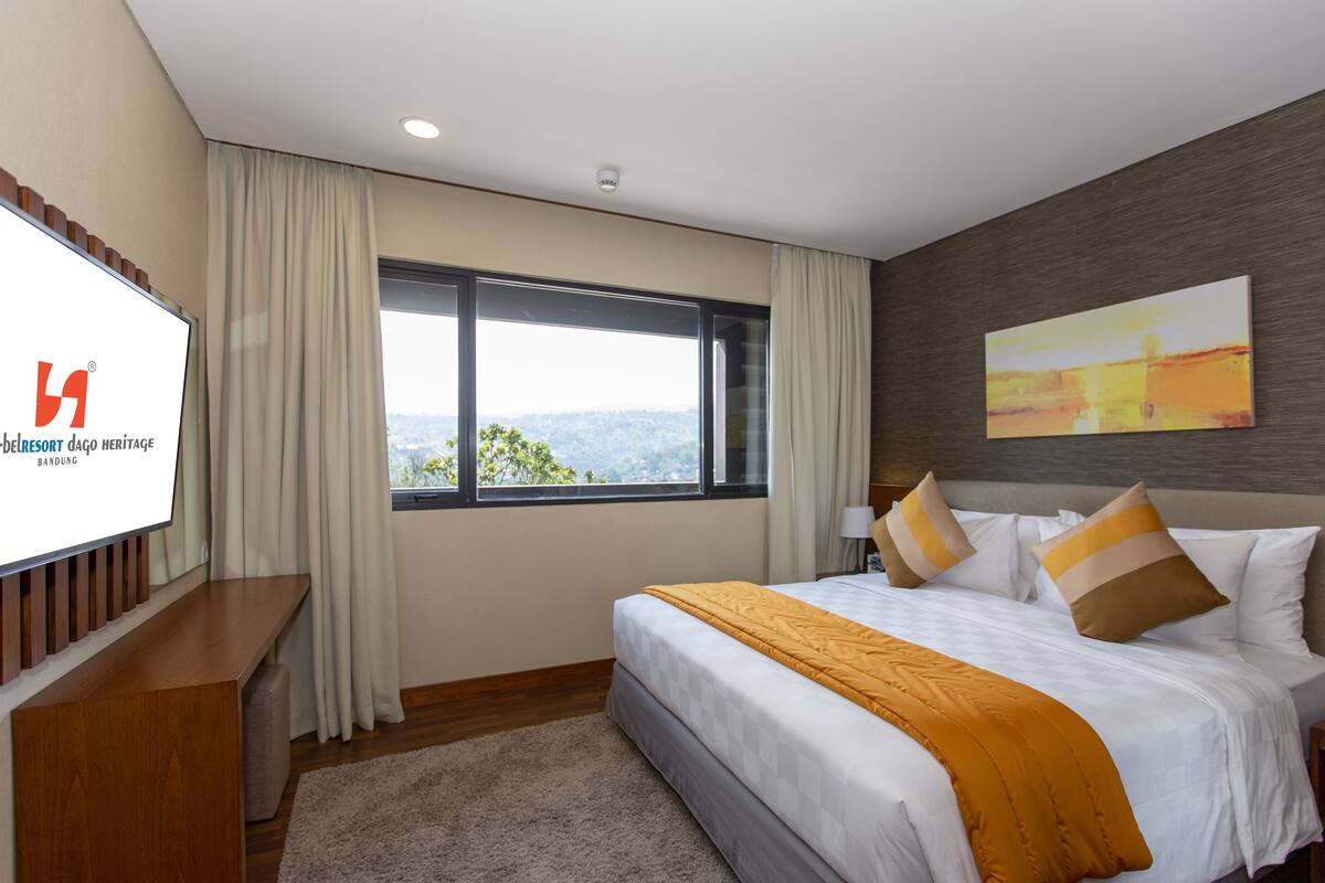 Una habitación de hotel con una cama grande, un televisor sobre un soporte de madera, una ventana con vistas y un cuadro en la pared.