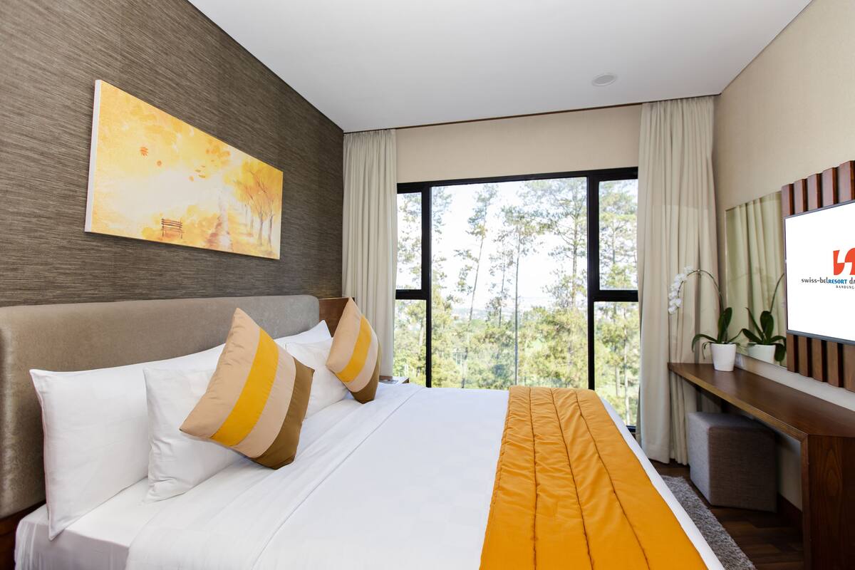 Habitación de hotel moderna con una cama grande, un escritorio y vistas a árboles por la ventana.