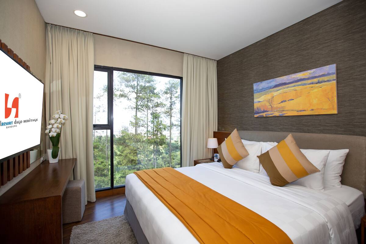 Una habitación de hotel con una cama grande, un escritorio, un televisor y un ventanal con cortinas.