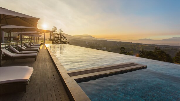 Una piscina d'hidromassatge infinita amb gandules i vista al capvespre sobre les muntanyes.